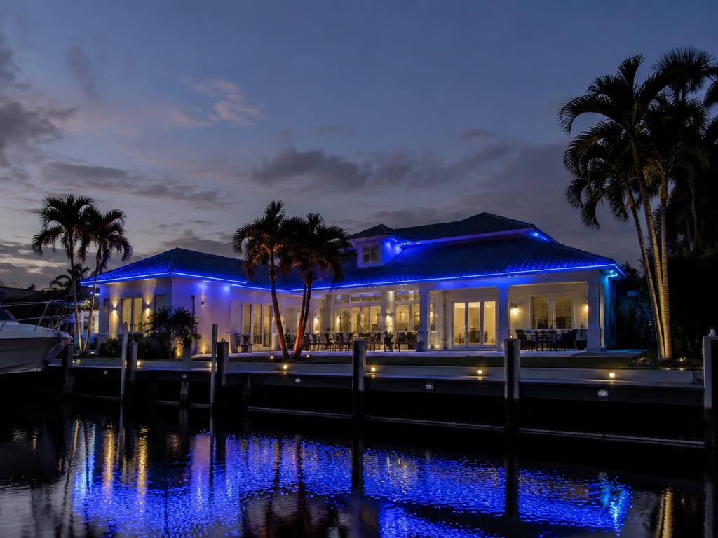 Florida waterfront home with permanent roofline lighting in a deep blue game-day color scene